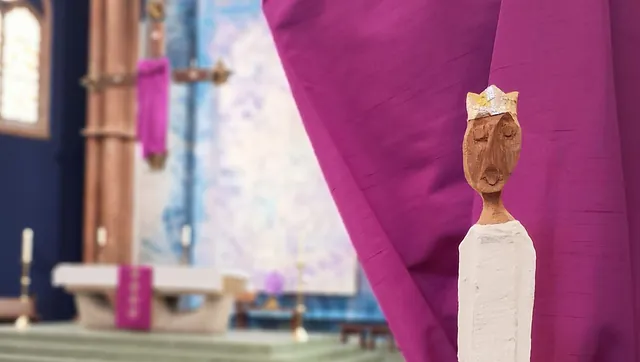 Eine Figur steht vor ein abgehängten Jesus-Kreuz in einer Kirche 