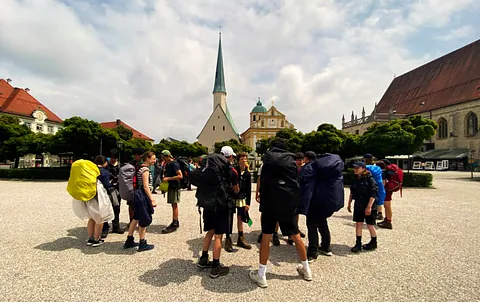 Pilger mit Rucksäcken stehen vor der Kirche in Altötting