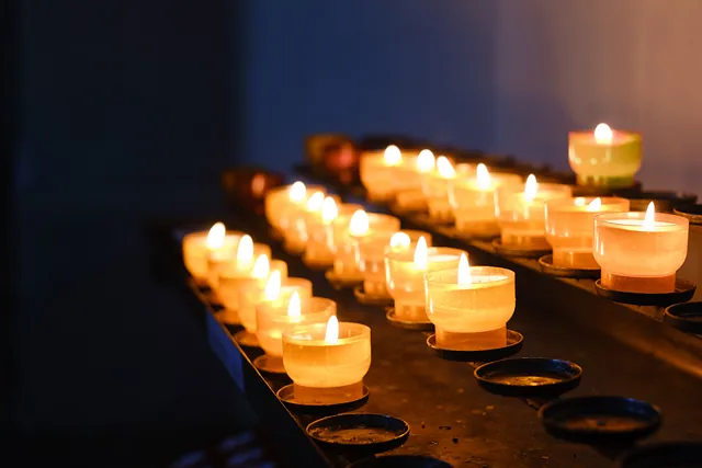 Leuchtende Kerzengläser auf einem Opferlichter-Ständer in der Nahaufnahme. 