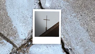 Ein Polaroid-Foto von einem Kreuz liegt auf dem Asphalt.