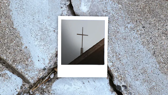 Ein Polaroid-Foto von einem Kreuz auf einem Dach liegt auf dem Asphalt.