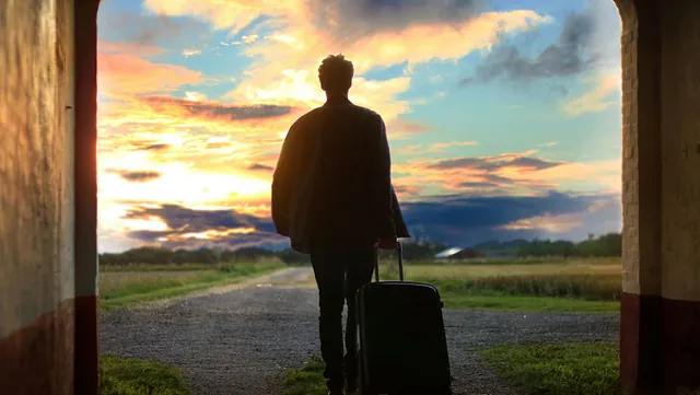 Ein Man mit Koffer läuft Richtung Horizont.