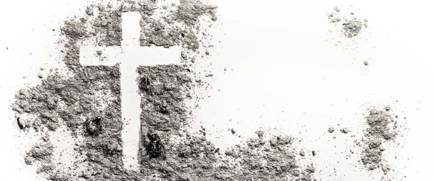 Asche auf einem weissen Hintergrund verteilt und ein Kreuz hinein gemalt 