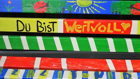 Bunt bemalte Banklatten mit dem Text „Du bist wertvoll“ und fröhlichen Motiven. 