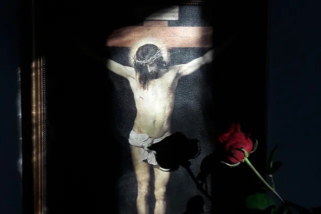 Ein Foto von Jesus am Kreuz mit einer roten Rose daneben. 