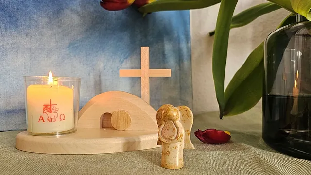 Ein Still leben aus einer kleinen Osterkerze, einem hölzernen Grabhügel mit Kreuz und einem kleinen Engel