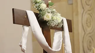 Geschmücktes Kreuz mit weißer Schärpe und weißen Rosen