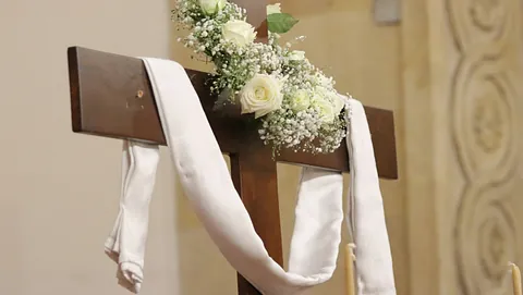 Geschmücktes Kreuz mit weißer Schärpe und weißen Rosen